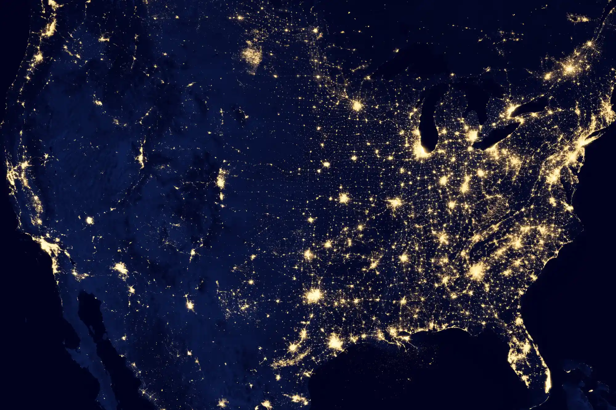 Satellite night view of the United States showing clusters of city lights highlighting population density, economic activity, and urban networks across the country.